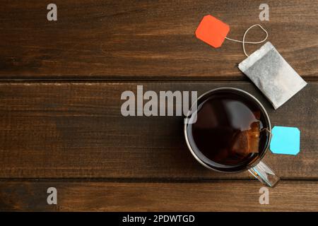 Sachets de thé dans une tasse d'eau chaude en verre sur une table en bois, plat. Espace pour le texte Banque D'Images