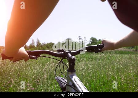 Vélo dans le parc de la ville. Vue à travers les yeux des motards. Mains sur le guidon d'une bicyclette gros plan Banque D'Images