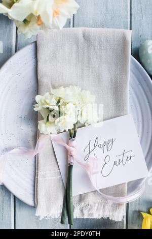 Un lieu de vacances avec une assiette, une serviette et une carte sur une table décorée pour Pâques. Prise de vue à partir de la position de pose à plat ou de la vue de dessus. Fleurs nouées avec du rose Banque D'Images