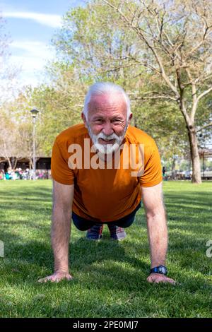 Portrait d'un homme âgé qui fait de l'exercice, qui fait des exercices dans le parc. Un homme âgé en bonne forme et en bonne santé avec des bras forts. Banque D'Images