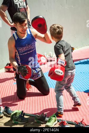 Khabarovsk, Russie - 20 mai 2017: Jeune boxeur asiatique formant un petit enfant à Muay Thai. Petit garçon en gants de boxe s'exerçant avec un entraîneur dans une salle de gym Banque D'Images