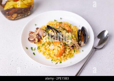 Risotto aux fruits de mer au safran et au persil. Riz Arborio aux crevettes tigrées, aux moules et au poulpe. Plats italiens traditionnels. Gros plan, foyer sélectif Banque D'Images