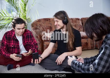 Les gars de la génération du millénaire communiquent assis sur le tapis avec les smartphones dans leurs mains Banque D'Images