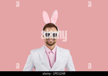 Jeune homme caucasien heureux avec des oreilles de lapin drôles sur la tête vêtu d'un costume blanc classique Banque D'Images