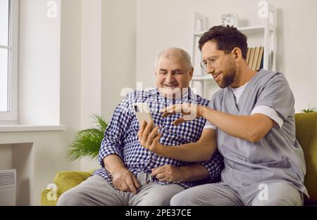 Jeune infirmière brune aidant un patient âgé à utiliser un smartphone. Banque D'Images