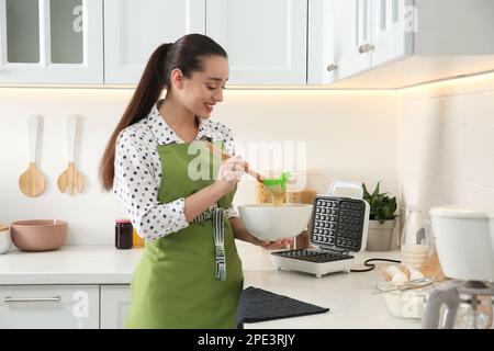 Femme préparant de la pâte près du gaufrier belge dans la cuisine Banque D'Images