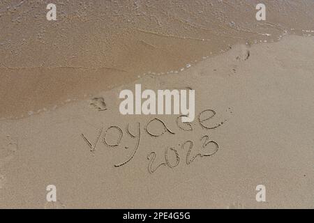 L'inscription voyaje 2022 en français, Voyage 2022, sur le sable par l'eau et la vague montante, mer vacances plage au bord de la mer. Banque D'Images