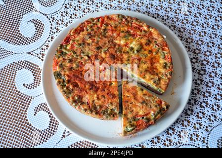 Une frittata italienne faite d'œufs, de viande, de fromage et de légumes sur une assiette sur une table avec nappe blanche. Un foo maison frais, délicieux et sain Banque D'Images