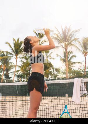 Femme joueur de tennis boire de l'eau à la bouteille pendant l'entraînement de tennis dans le climat tropical. Banque D'Images