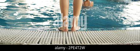 Bannière. Les pieds des femmes sur la marche à l'entrée de la piscine en fibre de verre avec de l'eau bleue dans le spa du complexe. Parquet blanc en teck ou en mélèze. Photo de haute qualité Banque D'Images