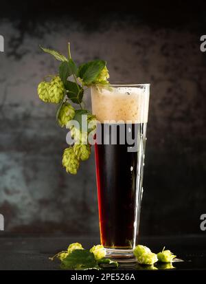 bière foncée dans une tasse et houblon vert sur une table en bois sur fond marron. Le concept de la bière naturelle. Les traditions de brassage. Oktoberfest. Festival de la bière. Banque D'Images