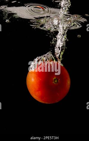 Tomate mûre tombe profondément sous l'eau avec un grand bruit. Banque D'Images
