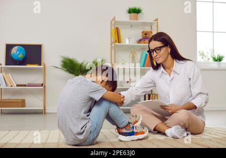 Frustré et confus adolescent assis sur le sol dans une posture fermée près du psychologue de l'école. Banque D'Images