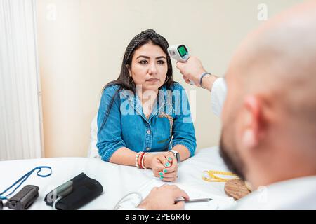 Médecin prenant de la température à la patiente dans le bureau. Médecin de sexe masculin prenant la température avec un pistolet jusqu'au patient. Médecin mesurant la température à l'infrarouge Banque D'Images