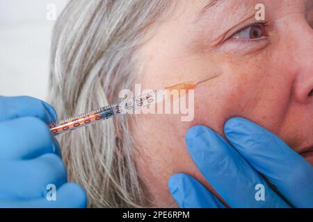 Gros plan d'un cosmetologists mains injectant le botox dans le visage d'une femme plus âgée avec des rides Banque D'Images