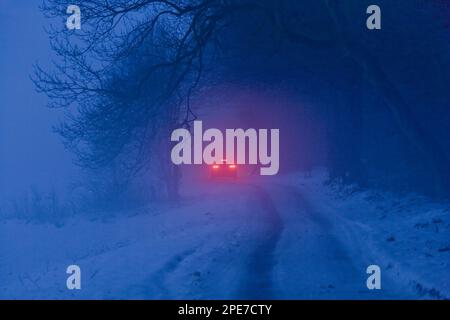 Feux de stop éloignés d'une voiture sur une route enneigée dans un brouillard givrant au crépuscule, Ampleforth, North Yorkshire, Angleterre, décembre 2009 Banque D'Images