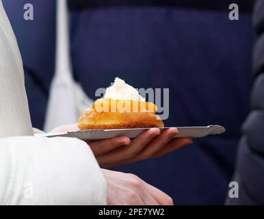 Un visiteur du marché agricole tient un plateau en papier avec un dessert acheté, un beignet avec de la gelée de fruits et de la crème fouettée. Banque D'Images