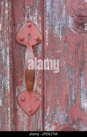 Gros plan de la poignée métallique rouge peinte sur l'ancienne grange avec peinture écaillée. Situé en Nouvelle-Angleterre. Banque D'Images