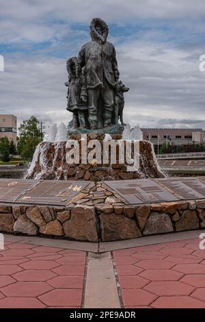 Fairbanks, Alaska, États-Unis - 27 juillet 2011 : statue et fontaine de la première famille inconnue. Gros plan du côté père avec l'enfant et le chien sous un paysage bleu. PLA Banque D'Images