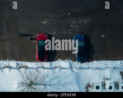 Une photo aérienne directement au-dessus de deux voitures Tesla Model 3 garées, rouges et bleues, à une station Tesla Supercharger en hiver. Banque D'Images