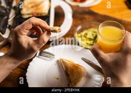 Un homme méconnaissable mange du pain grillé sur une assiette. Heure du petit déjeuner. Les mains de l'homme tiennent un couteau et une fourchette. Banque D'Images