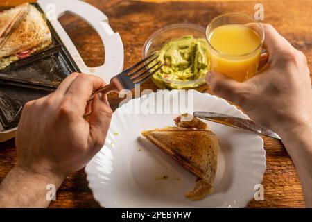 Un homme méconnaissable mange du pain grillé sur une assiette. Heure du petit déjeuner. Les mains de l'homme tiennent un couteau et une fourchette. Banque D'Images