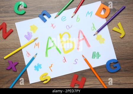 Feuille de papier avec l'abréviation ABA (Applied Behavior Analysis), lettres en plastique et crayons sur table en bois, plat Banque D'Images