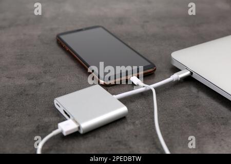 Smartphone moderne et ordinateur portable se recharge depuis la batterie portable sur une table grise, en gros plan Banque D'Images