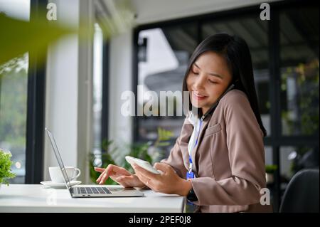 Une femme d'affaires ou une comptable féminine asiatique attirante et professionnelle est au téléphone avec son client d'affaires tout en utilisant la calculatrice et l'WO Banque D'Images