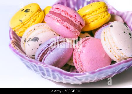 Macarons doux macarons dans un bol sur fond blanc. Petits gâteaux français à la vanille, à la framboise, au citron et à la fraise. Carte de pâtisserie Banque D'Images