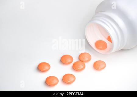 Pilules orange renversées du médicament d'ordonnance ouvert plastique blanc bouteille fond gris Banque D'Images