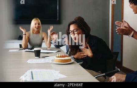 Jeune femme d'affaires célébrant son anniversaire au travail avec ses collègues. Femme soufflant des bougies sur un gâteau à la table de réunion du bureau, avec elle c Banque D'Images