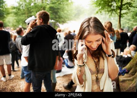 Dépêchez-vous, cet endroit est génial. Une jeune femme qui a du mal à entendre sur son smartphone lors d'un festival en plein air. Banque D'Images