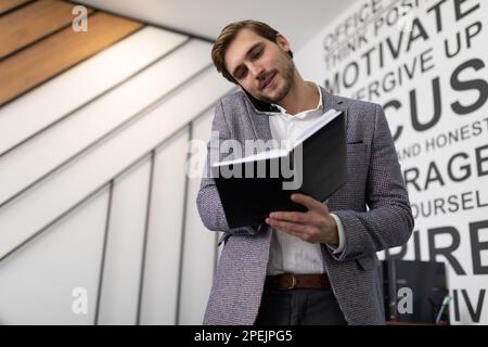 un travailleur d'affaires discutant de son activité au téléphone en tenant un bloc-notes entre ses mains Banque D'Images