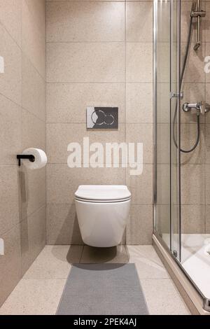 Vue directe de la petite salle de bains avec toilettes murales blanches et douche en verre avec carrelage beige élégant. Concept d'un élégant mais simple et concis Banque D'Images