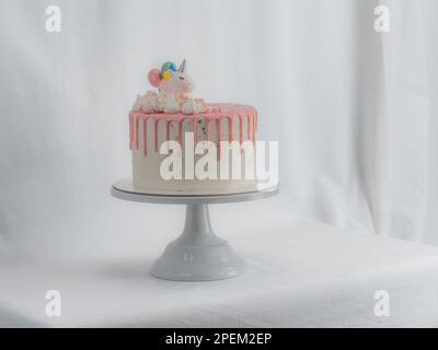 gâteau d'anniversaire blanc givré rose givré avec licorne, meringue et saupoudrés, peinture comestible dorée coups de pinceau sur le support Banque D'Images