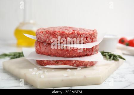 Patties de hamburger crues avec romarin et sel sur table en marbre blanc, gros plan