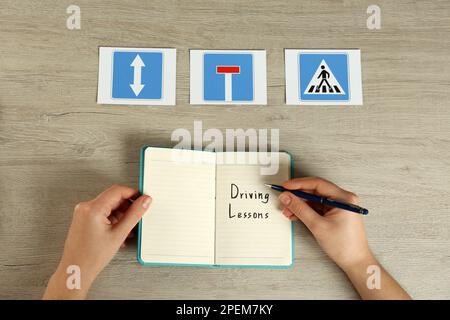 Femme avec guide pour leçons de conduite et panneaux routiers à la table en bois, vue de dessus. Réussite de l'examen de licence Banque D'Images