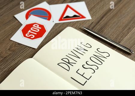 Manuel de cours de conduite, stylo et panneaux routiers sur table en bois, gros plan. Réussite de l'examen de licence Banque D'Images