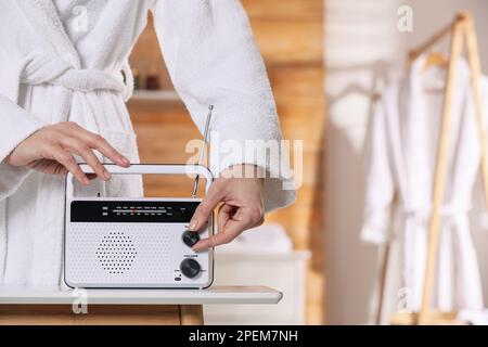 Femme en peignoir tournant le bouton de volume de la radio à l'intérieur, gros plan. Espace pour le texte Banque D'Images