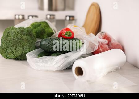 Rouleau de sacs en plastique et légumes frais sur table blanche Banque D'Images