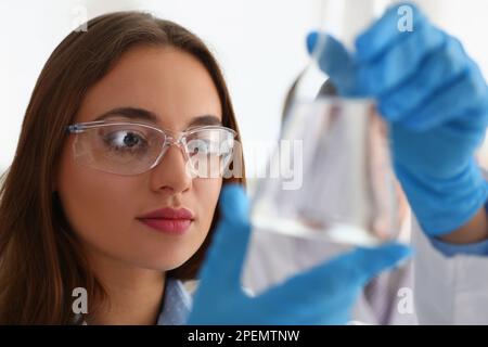 Portrait d'une femme scientifique dans des verres tient flacon avec liquide transparent Banque D'Images