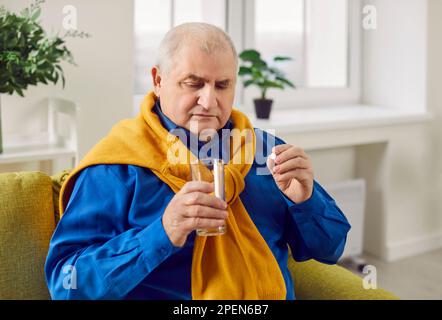 Retraité, homme âgé avec des problèmes de santé prend une pilule médicale avec un verre d'eau Banque D'Images