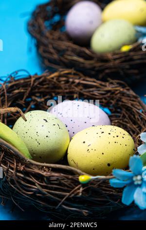 Oeufs de Pâques dans des paniers de nid en osier sur fond bleu. Banque D'Images