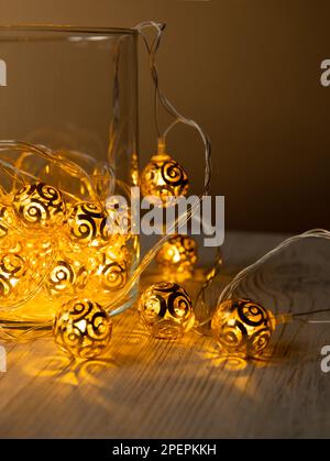 Guirlande de boules en métal doré dans un pot en verre sur fond de table en bois clair. Guirlande lumineuse de Noël jaune or avec ampoules LED. La guirlande du nouvel an. Pour Banque D'Images