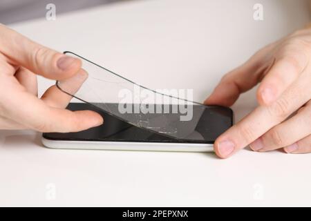 L'homme retire l'ancien verre de protection fissuré du téléphone. Verre de protection cassé Banque D'Images