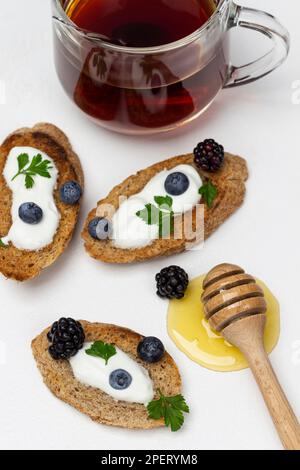 Croûtons à la crème et aux baies. Miel et bâton de miel. Une tasse de thé. Arrière-plan blanc. Banque D'Images