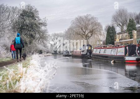 Matin froid, glacé, glacial par le canal britannique. Les bateaux sont amarrés le long d'un côté, les gens marchant avec le chien le long du chemin de halage. Voies navigables britanniques gelées en hiver Banque D'Images