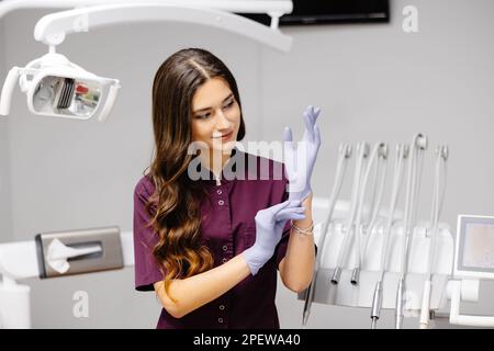 Femme blanche dentiste mettant des gants chirurgicaux stérilisés bleus dans la clinique médicale Banque D'Images