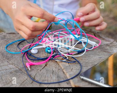 Un téléphone et une main tenant un nœud de quatre paires d'écouteurs intra-auriculaires filaires roses, bleus, blancs et noirs se sont emmêlés dans un problème désordonné. Banque D'Images